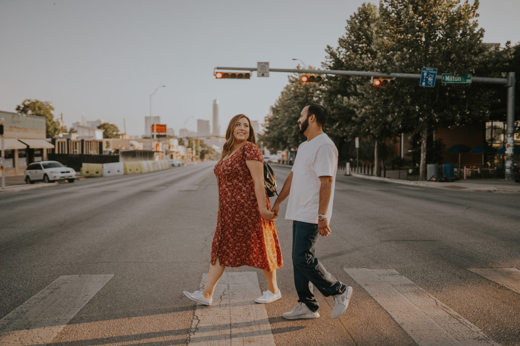 This is an engagement photo of a couple walking across South Congress Avenue.